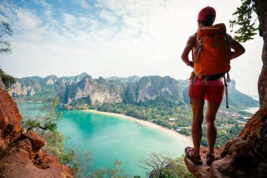 Sırt çantalı genç bir kadın deniz kenarındaki dağın tepesinde yürüyüş yapıyor..