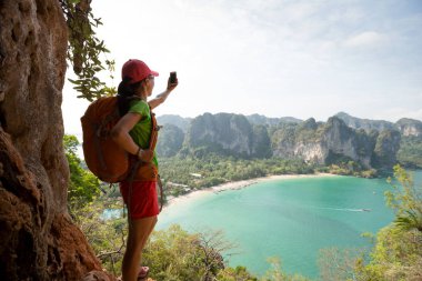 Genç bayan yürüyüşçü deniz kenarındaki dağ yamaçlarında selfie çekiyor..
