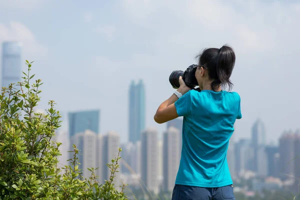在现代城市旁边的山上拍照的女摄影师 — 图库照片