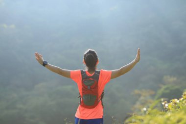 Tropikal orman yolunda kollarını açmış dişi ultramaraton koşucusunun arka görüntüsü.