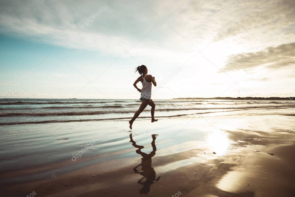 Young woman jogging at sunset on sandy beach in backlit