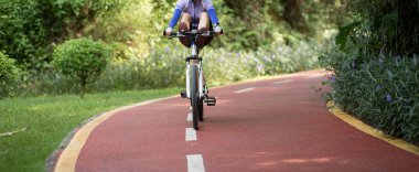 Parkta dağ bisikleti süren ve bacaklarıyla gidona çıkıp eğlenen bir kadın.