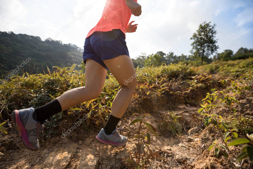 Woman ultramarathon runner running up on mountain slope in tropical forest 