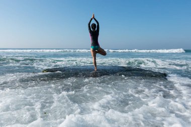 Deniz kenarındaki kayalıklarda yoga yapan kadın güçlü deniz dalgalarıyla karşılaşıyor.