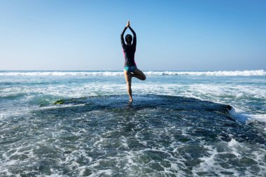 Deniz kenarındaki kayalıklarda yoga yapan kadın güçlü deniz dalgalarıyla karşılaşıyor.