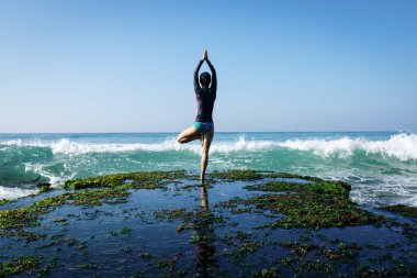 Deniz kenarındaki kayalıklarda yoga yapan kadın güçlü deniz dalgalarıyla karşılaşıyor.