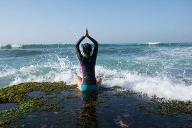 Deniz kenarındaki kayalıklarda yoga yapan kadın güçlü deniz dalgalarıyla karşılaşıyor.