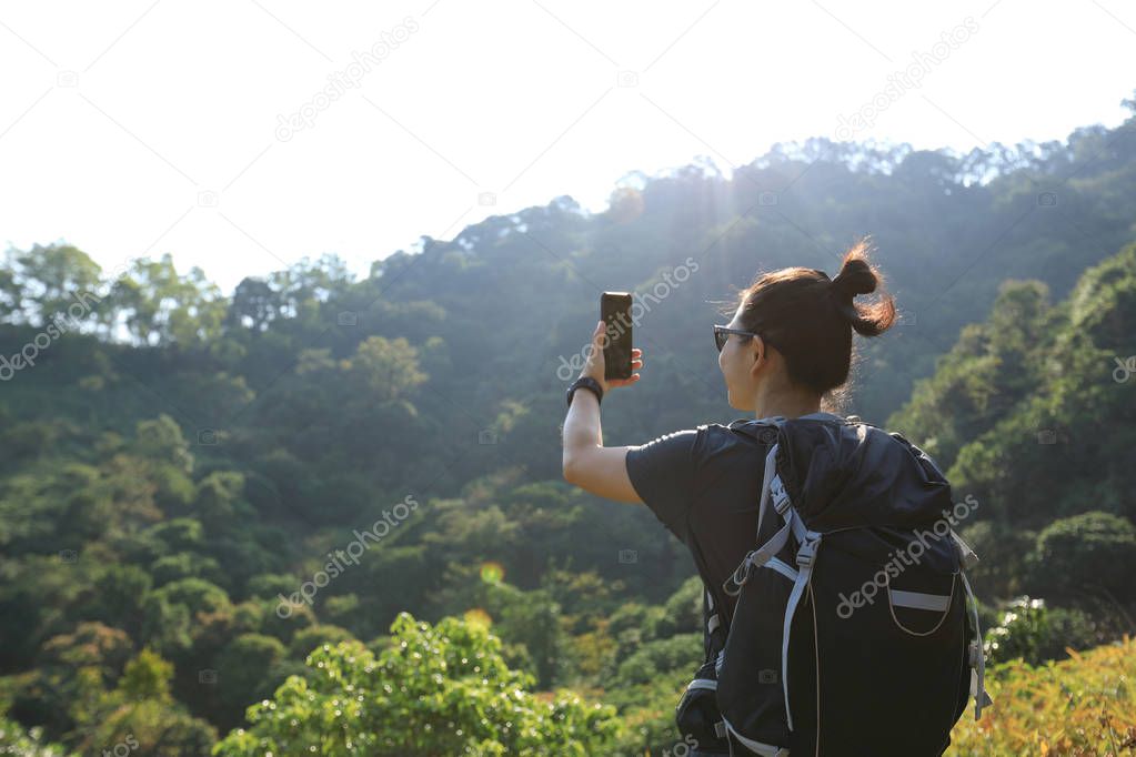 Female hiker taking photo with smartphone in autumn forest