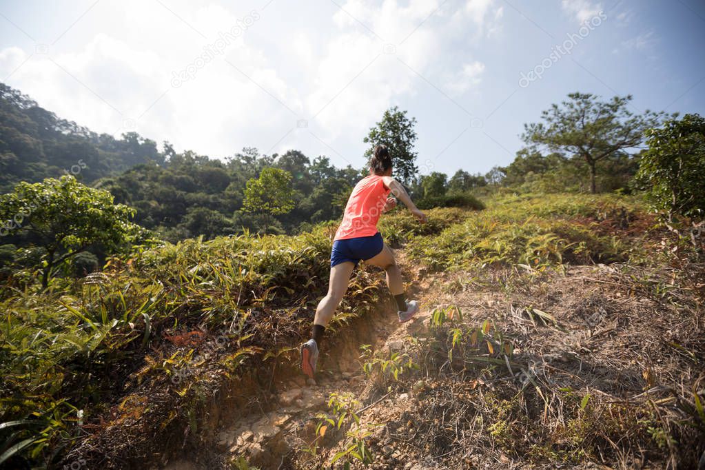Woman ultramarathon runner running up on mountain slope in tropical forest