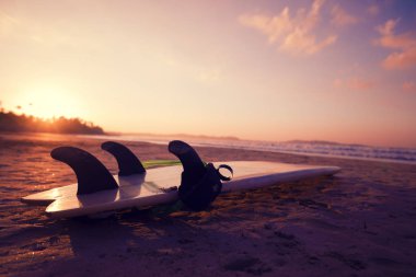 Yumuşak gündoğumunda kumlu sahilde sörf tahtası