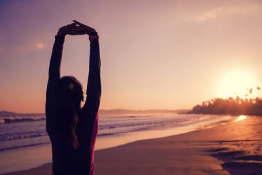 Fit dişi sörfçü sörf yapmadan önce sahilde ısınıyor.