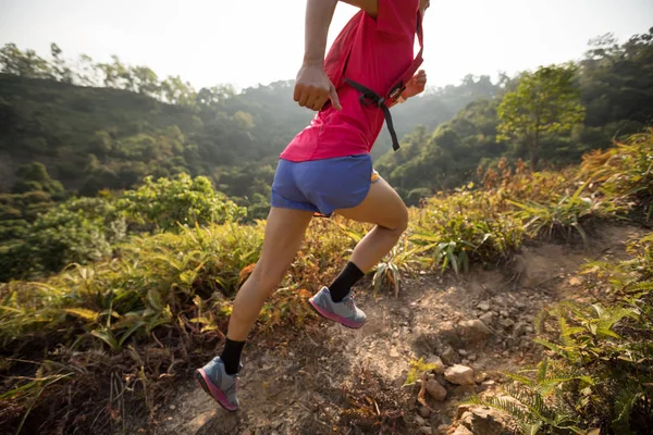 Female trail runner running up on mountain slope in tropical forest