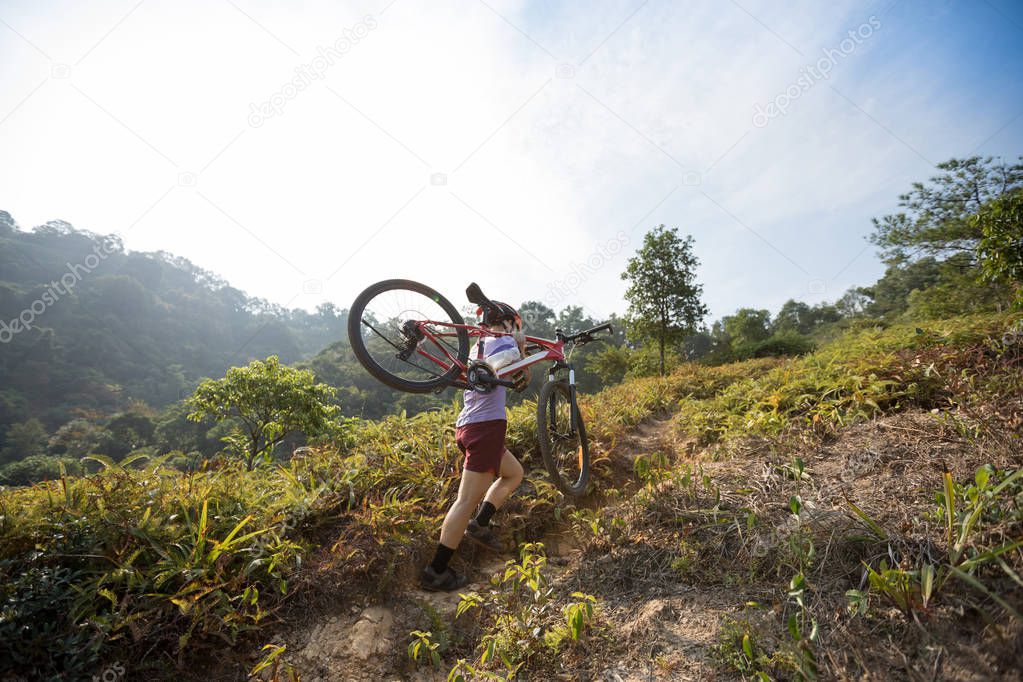 Cross country female cyclist carrying mountain bike on tropical forest trail