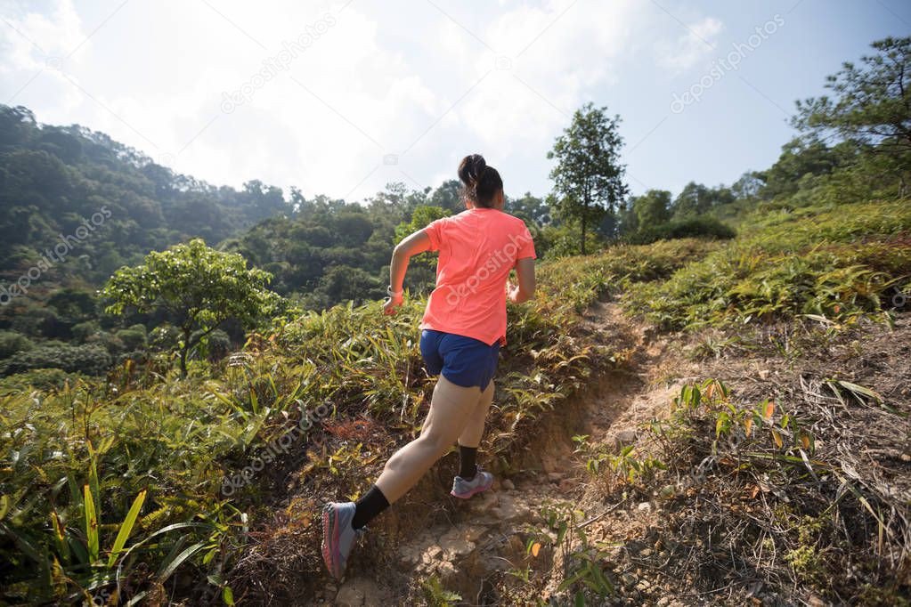 Woman ultramarathon runner running up on mountain slope in tropical forest 