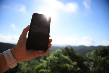 Güneş doğarken fotoğraf çekmek için cep telefonu kullanan bir el.