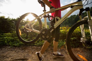 Tropikal ormanda dağda bisiklet taşıyan bir kadın bisikletçi.