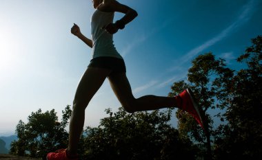 Fitness kadın koşucusu güneşin doğuşunda dağın tepesinde koşuyor.