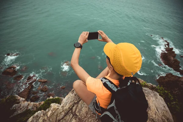 女徒步旅行者在海滨悬崖边用智能手机拍照 — 图库照片