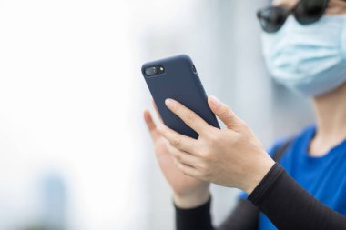 Yüz maskesi takan bir kadın şehirde akıllı telefon kullanıyor.