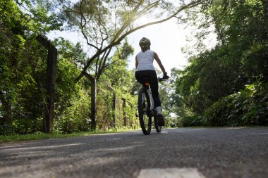 Güneşli bir günde parkta bisiklet süren bir kadın.
