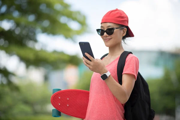 在现代城市 亚洲女子滑板手使用智能手机 — 图库照片