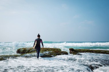 Sörf tahtası olan bir kadın deniz kenarında sörf yapacak.
