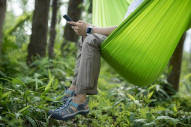 Tropikal ormanda akıllı telefon kullanarak hamakta dinleniyor.