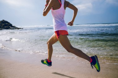 Genç fitness kadını gün doğumunda plajda koşuyor.