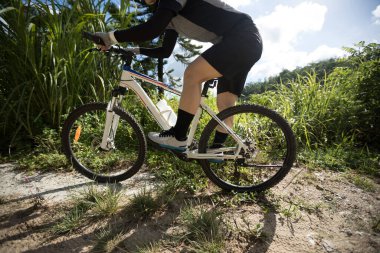 Güneşli bir günde yamaçta bisiklet süren bir kadın.