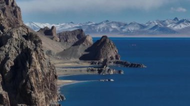 Açık gökyüzünün altındaki kayalık kayalıklarla çevrili derin mavi bir gölün çarpıcı videosu. Tibet, Çin  