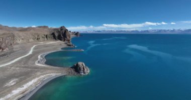 Açık gökyüzünün altındaki kayalık kayalıklarla çevrili derin mavi bir gölün çarpıcı videosu. Tibet, Çin  