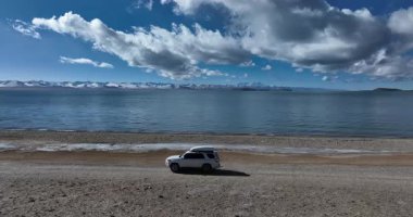 Çöl gölünde beyaz bir off-road arabası, bulutlu gökyüzü ve arka planda dağlar. 