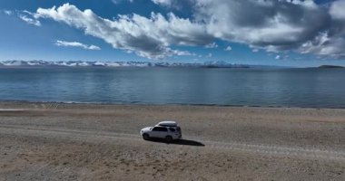 Çöl gölünde beyaz bir off-road arabası, bulutlu gökyüzü ve arka planda dağlar. 