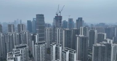Yüksek açılı bir video, modern apartman binaları ve yüksek vinçlerle yoğun bir şehir siluetini gösteriyor. Çin