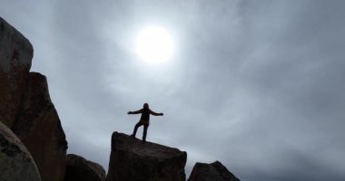 Bir gölün ve karlı dağların kenarındaki büyük kayalıklarda duran birinin arka videosu..