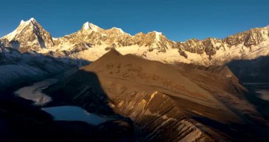 Geniş açılı bir video, uzun, karla kaplı dağları yansıtan geniş bir göl gösteriyor..