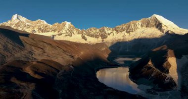 Geniş açılı bir video, uzun, karla kaplı dağları yansıtan geniş bir göl gösteriyor..