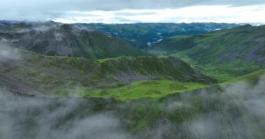 Bulutlu bir gökyüzü altında yemyeşil manzaralı puslu dağların hava görüntüleri.  