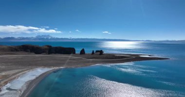 Yüksek açılı bir videoda engebeli, turkuaz bir göl ve kayalık bir uçurumun yanında.