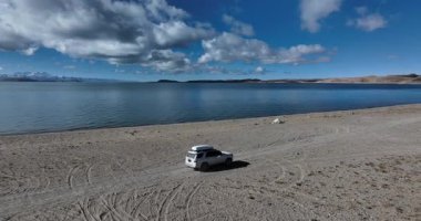 Çöl gölünde beyaz bir off-road arabası, bulutlu gökyüzü ve arka planda dağlar. 