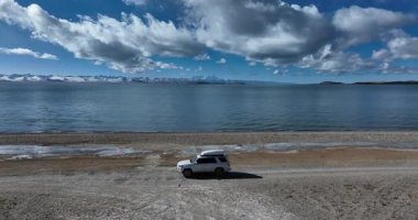 Çöl gölünde beyaz bir off-road arabası, bulutlu gökyüzü ve arka planda dağlar. 