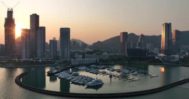 Video, şehir silueti üzerinde güzel bir gün batımı ve tekne dolu bir marina yakalıyor. 20 Mart 2025. Shenzhen şehri. Çin. 