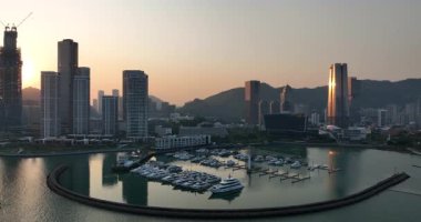 Video, şehir silueti üzerinde güzel bir gün batımı ve tekne dolu bir marina yakalıyor. 20 Mart 2025. Shenzhen şehri. Çin. 