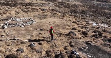 Sırt çantalı yalnız bir yürüyüşçü ve çorak bir dağ yamacında yürüyüş kıyafetleri. Yavaş çekim videosu 