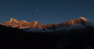 Gün batımında ay ışığıyla aydınlanan karlı dağlar.