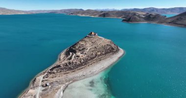 Tibet 'teki Yamdrok Gölü' nün canlı mavi sularının ön planda küçük, kurak bir adasıyla hava manzarası..