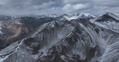 Bulutlu bir gökyüzünün altındaki karla kaplı sıradağların video görüntüleri..