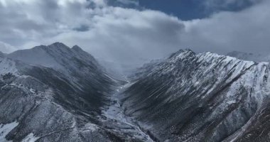 Bulutlu bir gökyüzünün altında karla kaplı bir dağ silsilesinin insansız hava aracı videosu.