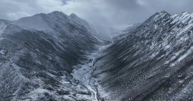 Karanlık, kayalık dağlar karla kaplı kasvetli, bulutlu ve sisli bir gökyüzünün altında.