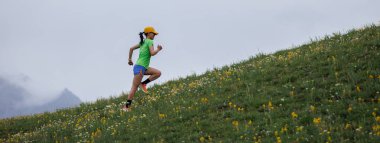 Yüksek dağ tepesinde koşan enerjik ve fiziksel olarak fit bir kadının panoramik çekimi.  